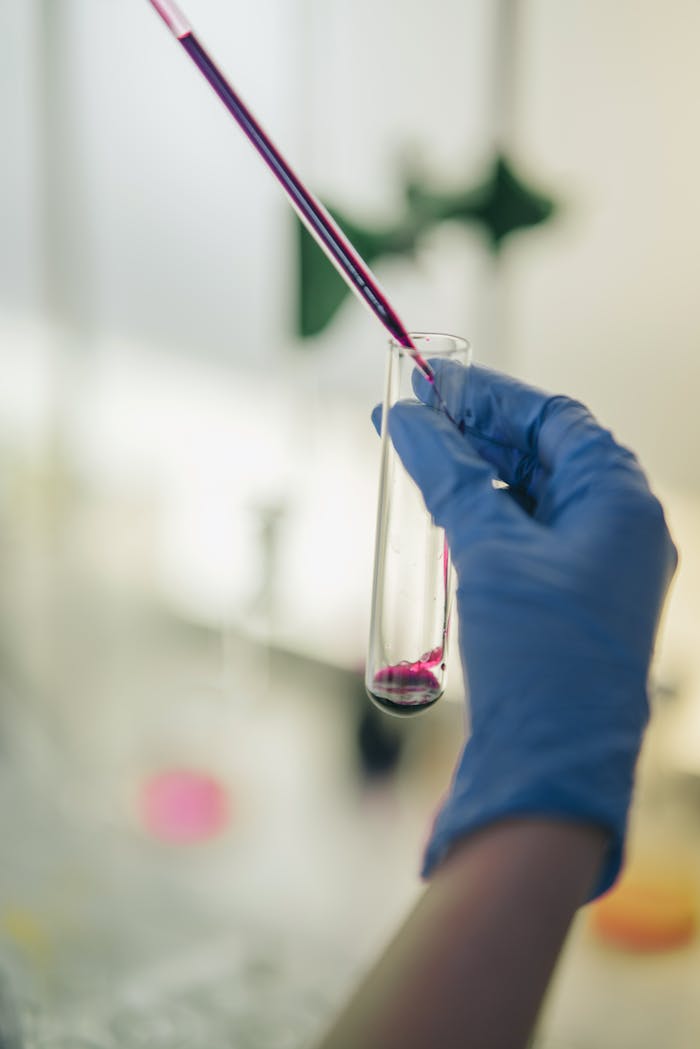 Close-up of a gloved hand using a dropper and test tube in a laboratory setting.